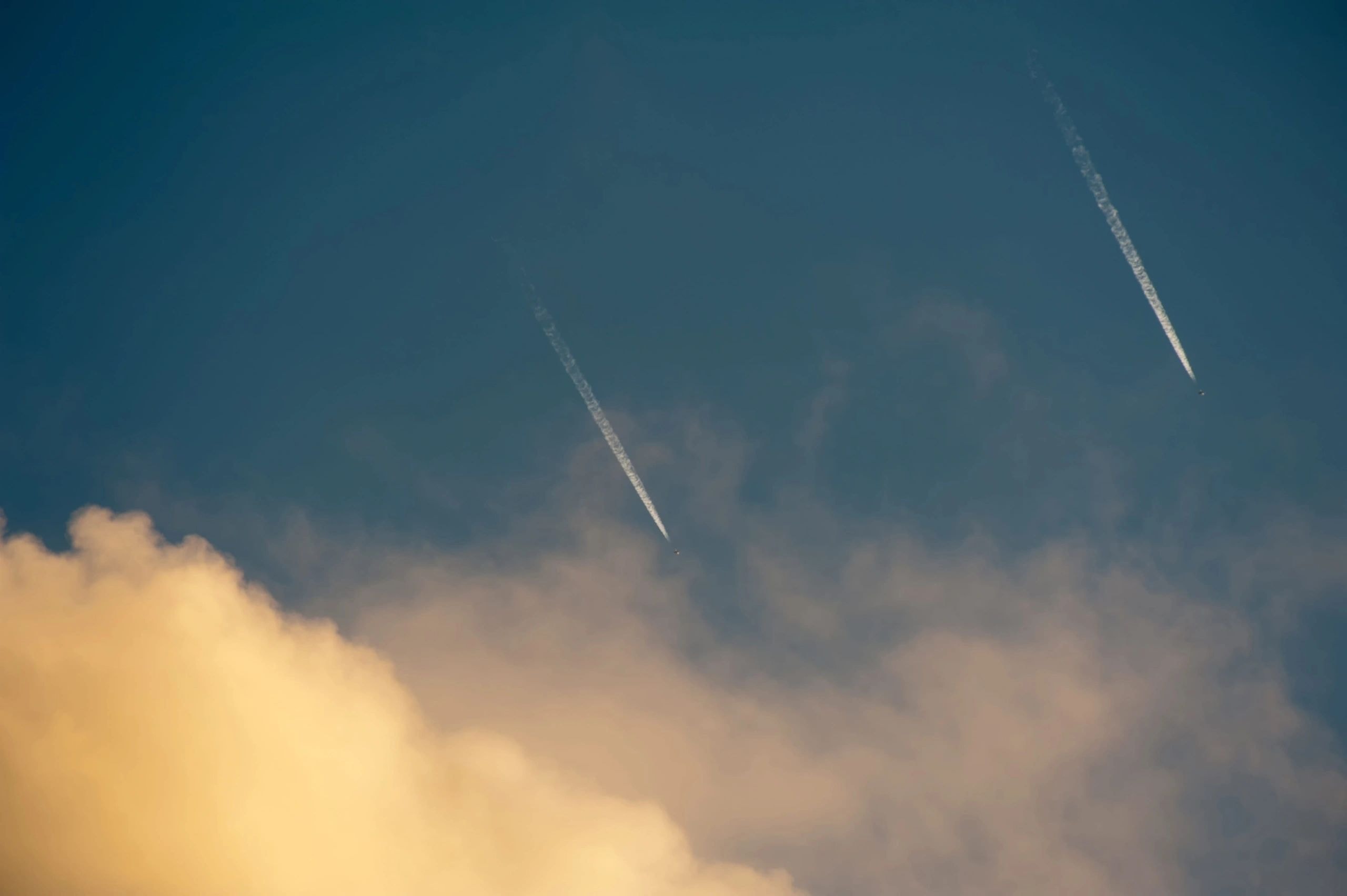 Two aircraft contrails streaking across a blue sky with golden clouds